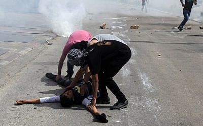 Palestinian demonstrators help an injured friend during clashes with Israeli security forces outside Ofer prison in the West Bank village of Betunia, on Thursday, May 16, 2014 (photo credit: AFP/Abbas Momani)