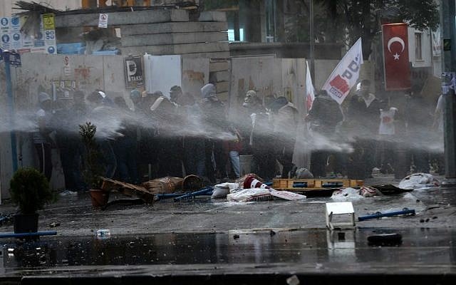 Protesters protect themselves from water cannons and tear gas fired by Turkish riot police on May 31, 2014 in Ankara, as they mark the first anniversary of last year anti-government demonstrations. Photo credit:AFP/ADEM ALTAN)