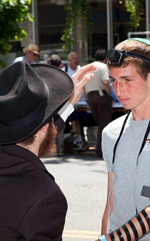 An Orthodox Jewish man helping a Jewish youth put on tefillin (phylacteries). (photo creit: Flickr/Robert Couse-Baker/CCBY-SA)