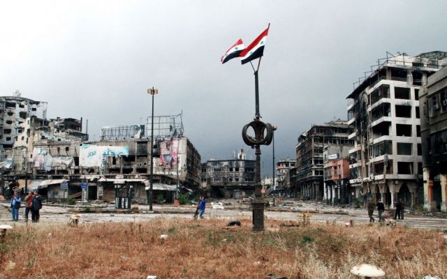 Two Syrian national flags hang on a pole as government officials inspect damages in the city of Homs, Syria, on May 8, 2014. (photo credit: AP)