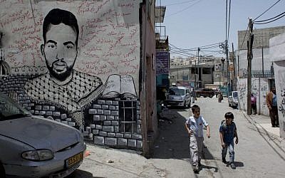 Two Palestinian school children walk past a mural depicting late Palestinian activist Ahmed Mosleh, who was killed during an Israeli army operation in 2006, with his name in Arabic and the names of other killed Palestinians, in an alley of the Dheisheh Palestinian refugee camp, in the West Bank city of Bethlehem, on Tuesday, May 20, 2014. (photo credit: AP Photo/Nasser Nasser)