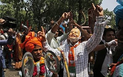 A Bharatiya Janata Party (BJP) supporter wears a mask of Narendra Modi, most likely India's next prime minister, after preliminary results showed the BJP winning by a landslide, outside the party headquarter in New Delhi, India, on Friday, May 16, 2014. (photo credit: AP/Manish Swarup)