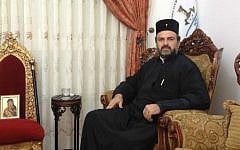 Father Gabriel Naddaf, in his living room, alongside a likeness of Mary, which, he believes, saved his life in a road accident in 2011. (Mitch Ginsburg/Times of Israel)