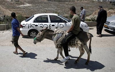 A Palestinian man rides his donkey past one of ten cars that were sprayed with racist slogans that read in Hebrew "All the Arabs are enemies" in the east Jerusalem neighborhood of Beit Hanina on June 23, 2014. (photo credit: Ahmad Gharabli/AFP)