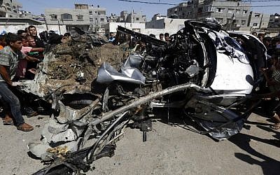 Palestinians gather around a car that was targeted by an Israeli air strike in Gaza City on June 27, 2014. (Photo credit: AFP/ MOHAMMED ABED)