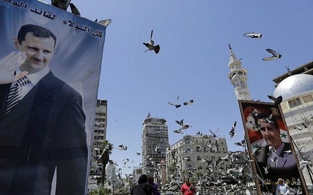 Syrians feed pigeons on a square where are displayed giant campaign billboards bearing portraits of Syrian President Bashar Assad on June 1, 2014 in the capital Damascus. (Photo credit: AFP/Joseph Eid) Syrians feed pigeons on a square where are displayed giant campaign billboards bearing portraits of Syrian President Bashar Assad on June 1, 2014 in the capital Damascus. (Photo credit: AFP/Joseph Eid)