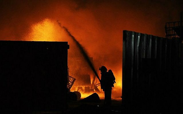 Israeli firefighters extinguish a burning factory hit by a rocket fired from the Gaza Strip on June 28, 2014 at an industrial zone in the southern city of Sderot. The previous day two Palestinians in the Gaza Strip were killed in an Israeli air raid after a bomb exploded near troops manning Israel's security fence. (photo credit: AFP/David Buimovitch)