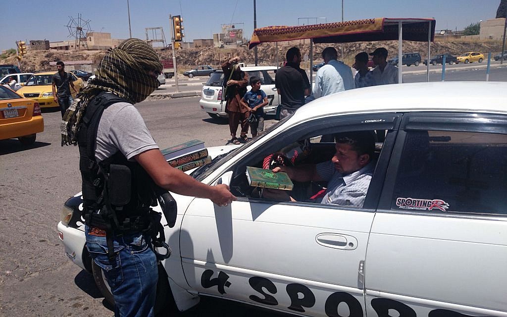 A fighter with the al-Qaida-inspired Islamic State of Iraq and the Levant (ISIL) distributes a copy of the Quran, Islam's holy book, to a driver in central northern city of Mosul, 225 miles (360 kilometers) northwest of Baghdad, Iraq, Sunday, June 22, 2014 (photo credit: AP) A fighter with the al-Qaida-inspired Islamic State of Iraq and the Levant (ISIL) distributes a copy of the Quran, Islam's holy book, to a driver in central northern city of Mosul, 225 miles (360 kilometers) northwest of Baghdad, Iraq, Sunday, June 22, 2014 (photo credit: AP)