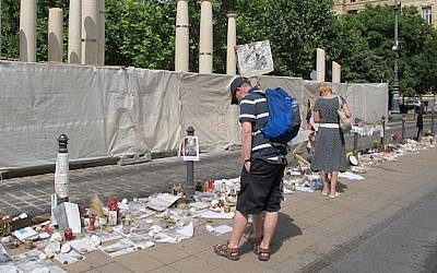 Passersby look at the Holocaust-related and other memorabilia left by citizens protesting the monument to the 1944 German occupation, under construction behind sheeting across the street in downtown Budapest. (Photo credit: JTA/Ruth Ellen Gruber)