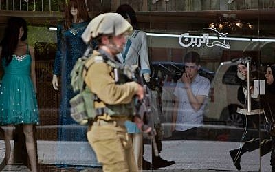 An IDF soldier walks on a street in a market in an attempt to obtain security camera footage during a search for three missing Israeli teens believed to have been abducted, while scouring the West Bank city of Hebron on Thursday, June 19, 2014. (AP Photo/Majdi Mohammed)