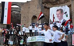 Supporters of Syrian President Bashar Assad hold his portraits and wave Syrian flags during a demonstration in support of his candidacy for presidential election in Suweida town, southern Syria, May 31 2014 (Photo credit: AP Photo/SANA)