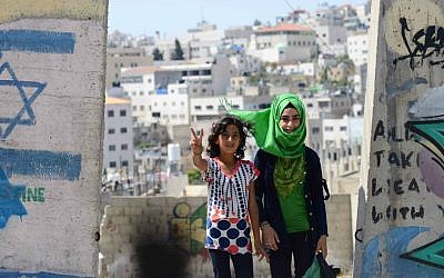 Young Arab children walk by a security wall painted with graffiti and and an Israeli flag, in the divided West Bank town of Hebron. June 24, 2014. (photo credit: Mendy Hechtman/FLASH90)