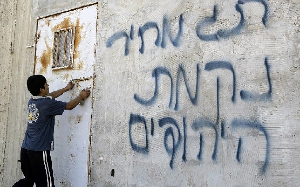 Illustrative: A Palestinian boy opens a door after Hebrew graffiti was daubed on a wall, allegedly by Jewish settlers, in the village of Aqraba, in the West Bank, close to the city of Nablus, on July 2, 2014 (AFP/JAAFAR ASHTIYEH)