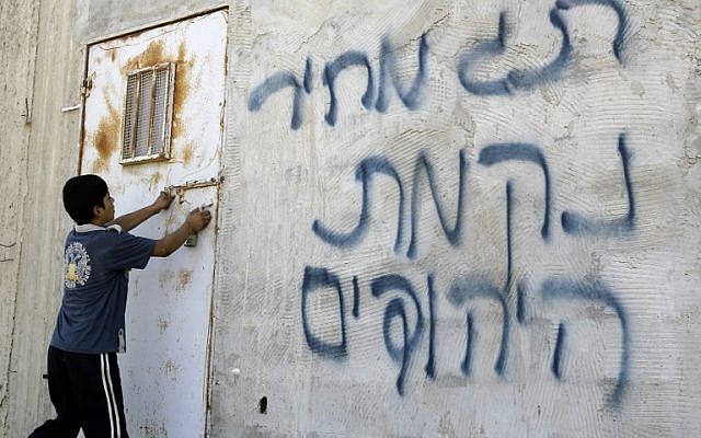 Illustrative: A Palestinian boy opens a door after Hebrew graffiti was daubed on a wall, allegedly by Jewish settlers, in the village of Aqraba, in the West Bank, close to the city of Nablus, on July 2, 2014 (AFP/JAAFAR ASHTIYEH) Illustrative: A Palestinian boy opens a door after Hebrew graffiti was daubed on a wall, allegedly by Jewish settlers, in the village of Aqraba, in the West Bank, close to the city of Nablus, on July 2, 2014 (AFP/JAAFAR ASHTIYEH)