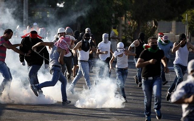 Palestinian protesters stand amid smoke after Israeli forces fired tear gas during clashes in Shuafat, East Jerusalem on July 4, 2014. (Photo credit: AFP/ THOMAS COEX)