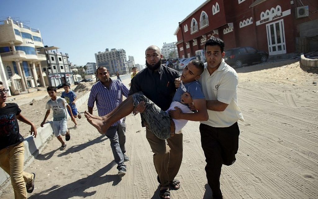 Palestinian employees of Gaza City's al-Deira hotel carry a wounded boy following an Israeli military strike near on the beach, on July 16, 2014. Four children were killed in Gaza City during the attack. (photo credit: AFP/THOMAS COEX)