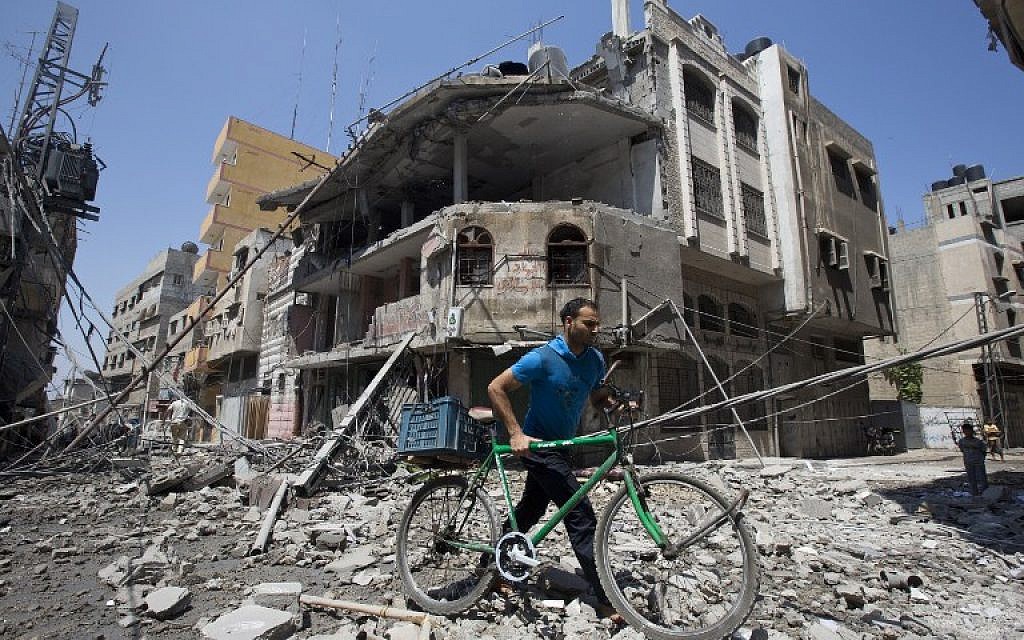 A Palestinian man pushes his bicycle amidst debris following an Israeli military strike in Gaza city, on July 23, 2014. (photo credit: AFP/ MAHMUD HAMS)