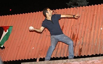 A demonstrator throws stones after climbing a wall with a Palestinian flag at the Israeli Embassy in Ankara during a protest against Israel's military action in Gaza, on July 18, 2014. (Photo credit: AFP/ADEM ALTAN)