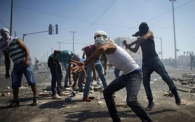 Masked Palestinian protesters throw stones towards Israeli police during clashes in the Shuafat neighborhood in East Jerusalem, July 3, 2014 (Photo credit: Thomas Coex/AFP)