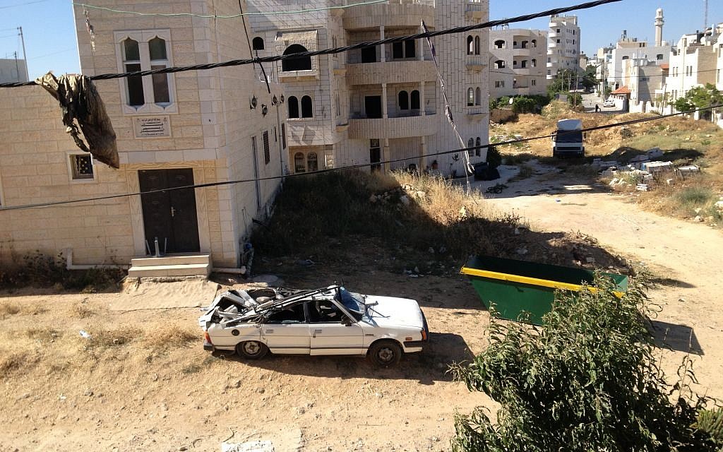 A car parked in the courtyard of the Abu Aysha home in Hebron was crushed by falling bricks from the building's wall and moved outside (photo credit: Elhanan Miller/Times of Israel)