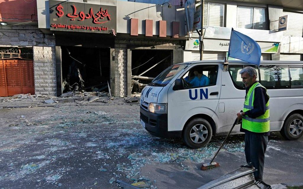 A Palestinian municipality worker sweeps glass from the street, as a UN vehicle drives past a damaged money-exchange post, following an overnight Israeli missile strike in Gaza City, Thursday, July 17, 2014. (photo credit: AP/Lefteris Pitarakis)
