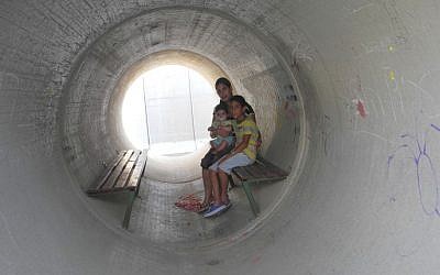 Devorah Israeli, of Nitzan, with 8-year-old Idan and 6-month-old Ron in the sewage pipe bomb shelter next to her home, which residents complain is not sufficient protection (photo credit: Melanie Lidman/Times of Israel)