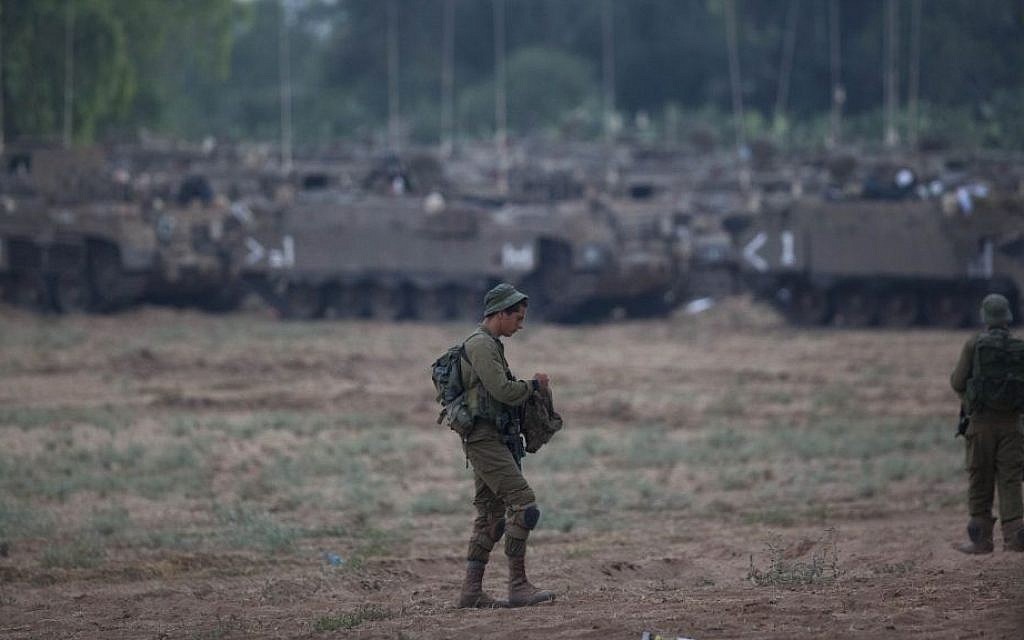 A soldier stands in a field near the Gaza border with IDF APCs (Armed Personnel Carriers) in the background, Wednesday, July 9, 2014. (photo credit: Yonatan Sindel/Flash90)