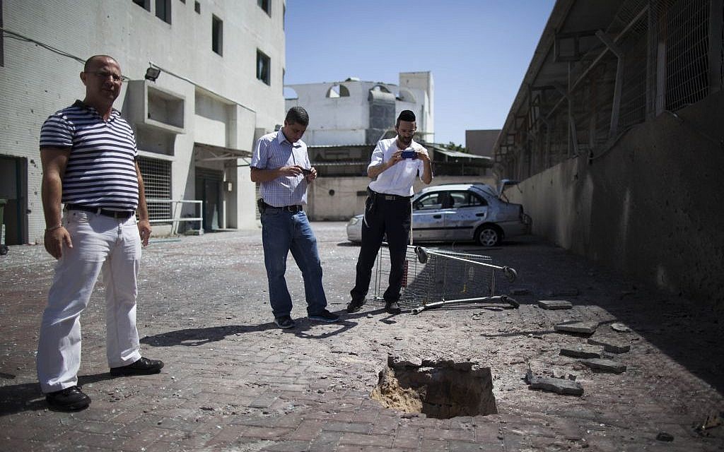 Israelis look at a crater caused by a rocket outside a shop in Ashdod, on the second day of Operation Protective Edge, Wednesday, July 9, 2014 (photo credit: Yonatan Sindel/Flash90)