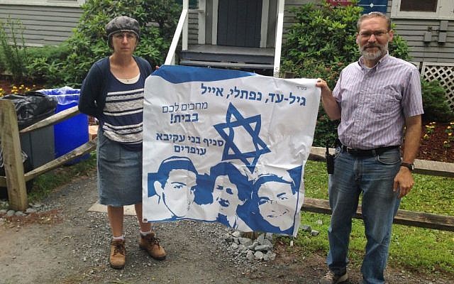 Camp Moshava's director, Alan Silverman, and its head counselor, Chanah Spiegelman, posing at the camp in Honesdale, Pa., with a banner expressing hope for the return home of three teenage Israelis who later were found to have been murdered. (Camp Moshava/via JTA)
