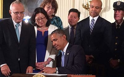 President Barack Obama signs an executive order extending work protection rights to LGBT employees of federal contractors, as Rabbi David Saperstein (left), director of the Religious Action Center of Reform Judaism, looks on, at the White House, on July 18, 2014. (Hadar Susskind/Bend the Arc via JTA)