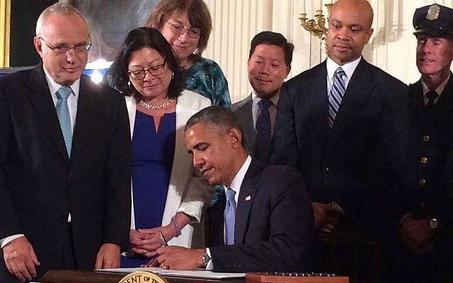 President Barack Obama signs an executive order extending work protection rights to LGBT employees of federal contractors, as Rabbi David Saperstein (left), director of the Religious Action Center of Reform Judaism, looks on, at the White House, on July 18, 2014. (photo credit: Hadar Susskind/Bend the Arc via JTA)