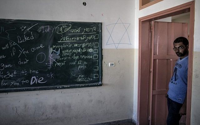 A Palestinian man stands near a blackboard scribbled with a Star of David, some military instructions in Hebrew and a map of a school after Israeli soldiers withdrew from the Beit Hanun High school for girls, Tuesday, August 5, 2014. (photo credit: Marco Longari/AFP)
