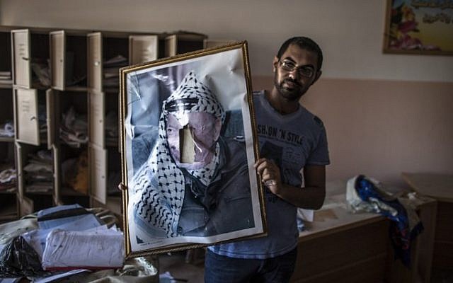 A defaced portrait of the late Palestinian leader Yasser Arafat is held by a man in a classroom after Israeli soldiers withdrew from the Beit Hanun High school for girls which was reportedly used as an advanced base during Israel's military offensive against Hamas, on August 5, 2014 (Photo credit: Marco Longari/AFP)