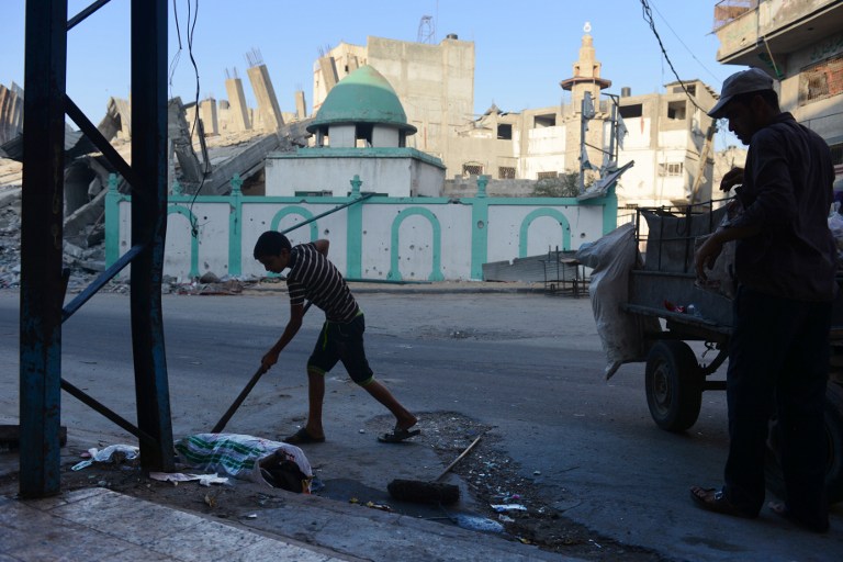 A Palestinian boy and his father clean garbage in the street across from the Omari mosque on August 12, 2014 in Jabalia, in the northern Gaza Strip. (photo credit: AFP/ROBERTO SCHMIDT) A Palestinian boy and his father clean garbage in the street across from the Omari mosque on August 12, 2014 in Jabalia, in the northern Gaza Strip. (photo credit: AFP/ROBERTO SCHMIDT)