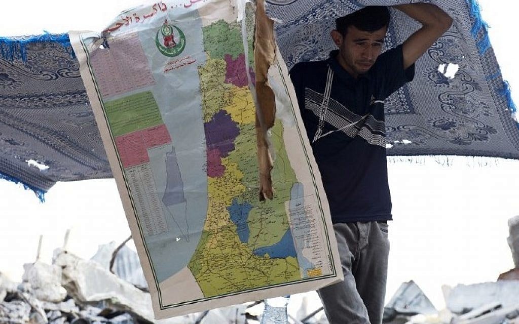 A Palestinian man is seen under a blanket and a map of Israel and the Palestinian Territories errected to give shade, as he walks over the rubble of what used to be a family home, in the Shejaiya neighborhood of Gaza City, on August 18, 2014.  (photo credit: AFP/ ROBERTO SCHMIDT)