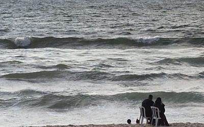 A Palestinian couple sit on plastic chairs as they watch their children play at a Gaza City beach on August 18, 2014. (photo credit: AFP Photo/Roberto Schmidt)