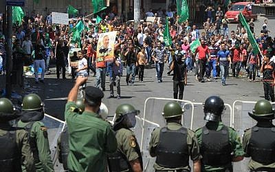 Palestinian demonstrators throw stones at Palestinian Authority security forces blocking the road to an Israeli checkpoint in the center of the West Bank town of Hebron on August 22, 2014, following a demonstration to show support for Hamas. (Photo credit: AFP/ Hazem Bader)