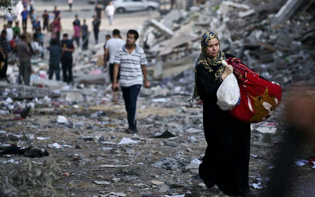 A Palestinian woman takes some of her belongings from her partially destroyed home across the street from where a high rise apartment building, that Israel said was used as a Hamas command center in Gaza City, was targeted by Israeli air strikes overnight on August 26, 2014.  (photo credit: AFP/ROBERTO SCHMIDT)
