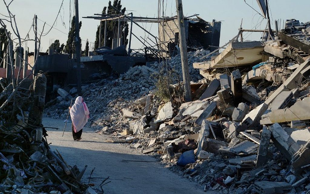 A Palestinian woman uses a piece of rebar she found amid the rubble, for support as she walks past destroyed homes in a street in Beit Hanoun, northern Gaza Strip, on August 12, 2014. (photo credit: AFP/ROBERTO SCHMIDT)