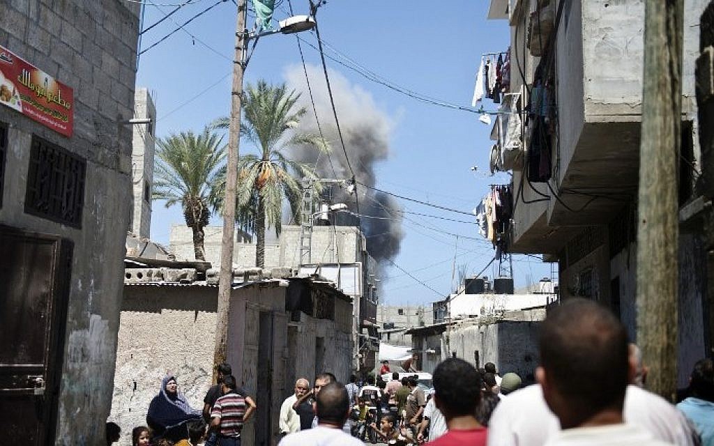 Palestinians watch as a cloud of smoke rises above local homes moments after an Israeli missile hit an open field nearby in Gaza City on August 21, 2014. (photo credit: AFP/ ROBERTO SCHMIDT)