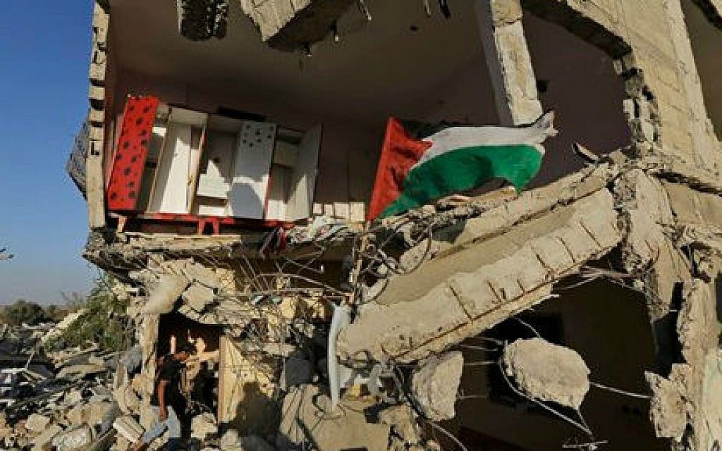 A Palestinian walks into a house, destroyed by an Israeli strike in the Gaza City neighborhood of Shejaiyah, a Hamas stronghold from which hundreds of rockets were fired at Israel, as the national flag flies on the rubble, Thursday, Aug. 7, 2014 (photo credit: AP/Lefteris Pitarakis)