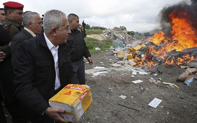 Former Palestinian prime minister Salam Fayyad throws a package into a fire set to burn products from Jewish settlements, in the West Bank of Salfit, January 5, 2010 (photo credit: AP/Nasser Ishtayeh)