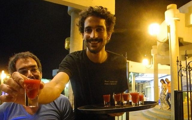 Ido Ozeri, one of the owners of Archies bar and restaurant in Ashkelon, passes out shots courtesy of a bar tab from American-Israeli Yigal Rechtman on Tuesday, the first night of the ceasefire. (photo credit: Melanie Lidman/Times of Israel)