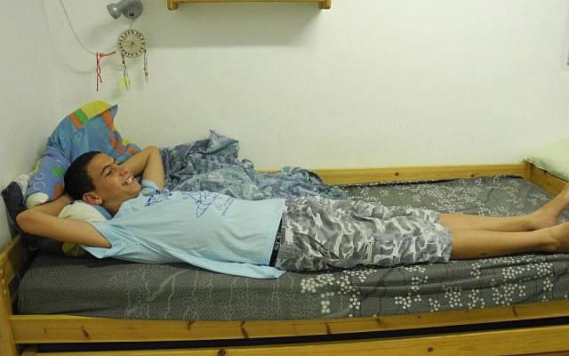 Regev Haglili, 14, smiles in his own bed after living for the past month with his mother and two brothers at Kibbutz Mishmar HaEmek in northern Israel. (photo credit: Melanie Lidman/Times of Israel)