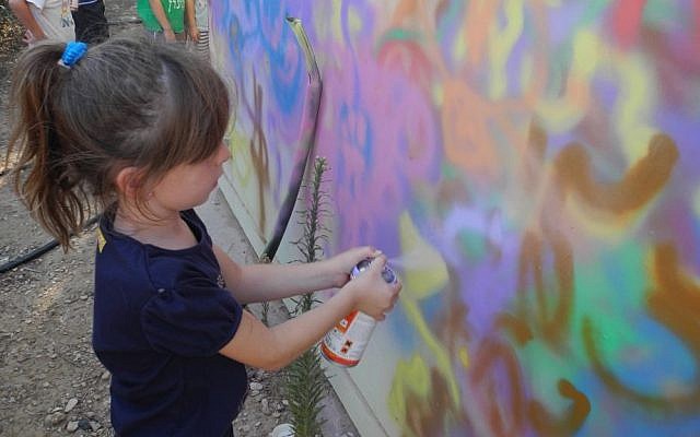 A girl at Kibbutz Alumim spray paints a bomb shelter with Artists 4 Israel. (Melanie Lidman/Times of Israel) A girl at Kibbutz Alumim spray paints a bomb shelter with Artists 4 Israel. (Melanie Lidman/Times of Israel)