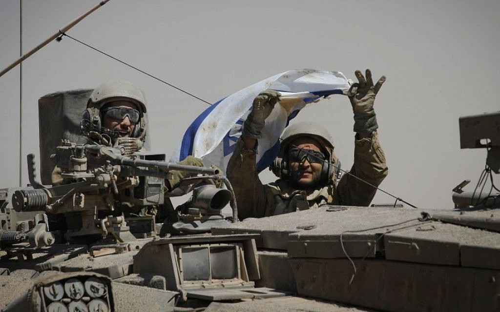 IDF soldiers hold up an Israeli flag as they ride in a tank along Israel's border with the Gaza Strip, Friday, August 1, 2014. (photo credit: Albert Sadikov/Flash90)