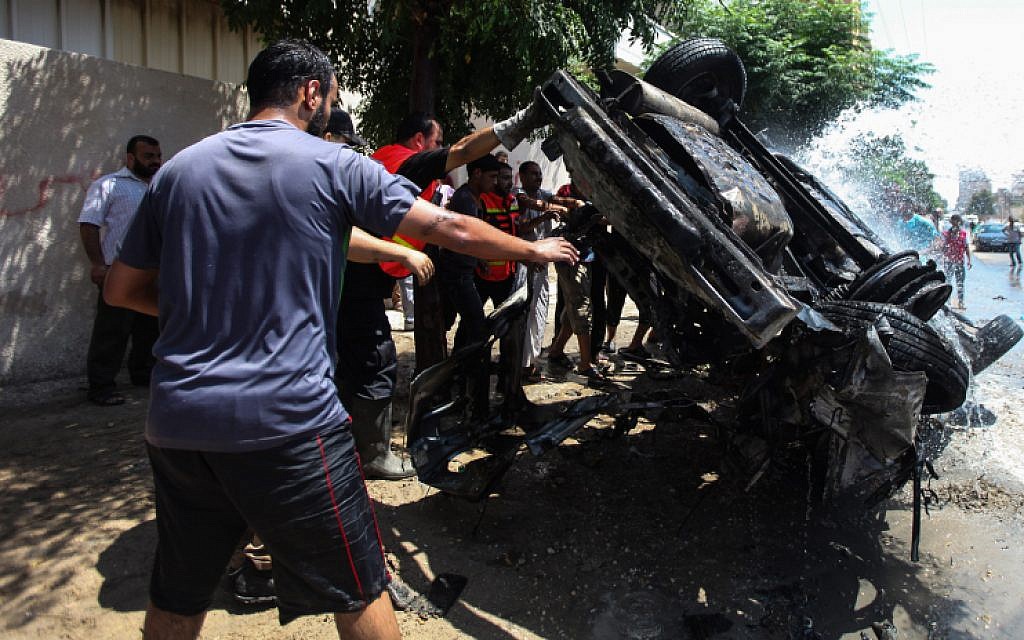 Palestinians around a destroyed vehicle after an Israeli airstrike in Gaza City on August 24, 2014. (photo credit: Emad Nassar/Flash90)