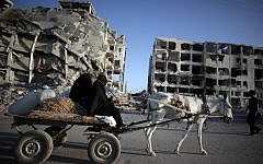 Two Palestinian women ride a donkey cart past the destroyed Nada Towers residential neighborhood in the town of Beit Lahiya, northern Gaza Strip, Monday, Aug. 11, 2014. (photo credit: AP Photo/Khalil Hamra)