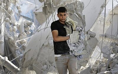 A Palestinian youth carries damaged copies of the Quran, Islam's holy book, found in the rubble of the Imam Al Shafaey mosque, destroyed in an overnight Israeli strike in Gaza City in the northern Gaza Strip on Saturday, Aug. 2, 2014. (Photo credit: AP/Lefteris Pitarakis)