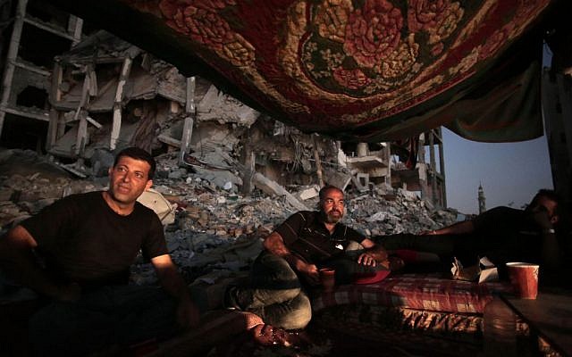 Palestinian Ziad Rizk, center, sits with others in a shelter made of a blanket stretched over four poles next to one of the destroyed al-Nada Towers, where he lost his apartment and clothes shop, in the town of Beit Lahiya, northern Gaza Strip.  (photo credit: AP Photo/Khalil Hamra, File)
